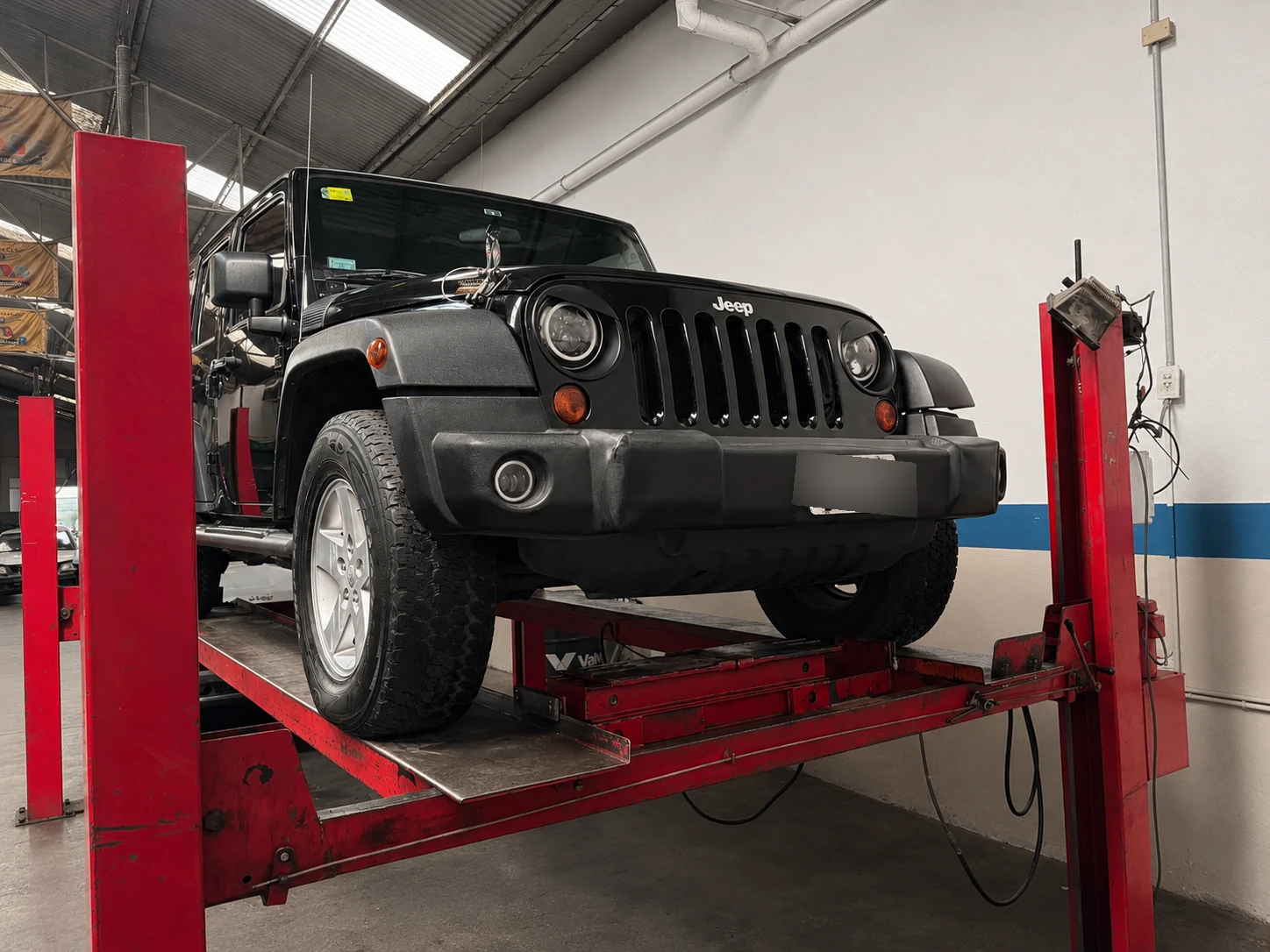 Jeep Wrangler Unlimited negra sobre el elevador de cuatro columnas en el taller mecánico Lomayler en Villa Crespo, CABA